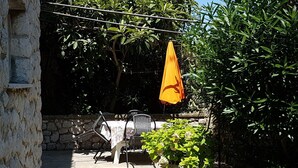 Een stenen muur, buitenzitplaats met een tafel en stoelen, en een oranje parasol.