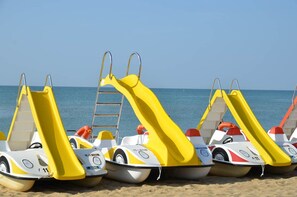 A row of small, yellow and white watercraft with slides on a sandy beach. - House in semi detached villa with garden (Bibione)