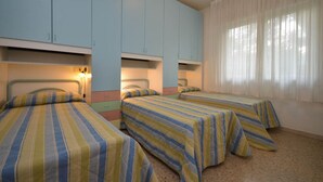 Ein Zimmer mit zwei Betten, hellblauen Schränken und einem großen Fenster mit leichtem Vorhang.