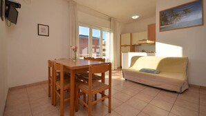A dining area with a wooden table and chairs, a sofa, and a kitchen in the background. - Nice two room apartment in Bibione (Bibione)