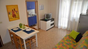 Un espacio habitable compacto con una mesa de comedor, sillas, kitchenette, televisor y una cama con colcha colorida.