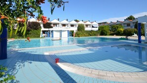 A swimming pool with tiled flooring, surrounded by a building with multiple balconies and a clear blue sky. - Villa with private garden and terrace (Bibione)