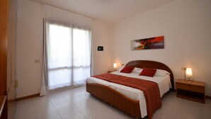A bedroom with a bed, a nightstand, a painting, and a window with curtains. - Villa with private garden and terrace (Bibione)