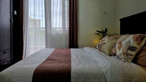Una habitación de hotel con cama, cortinas, unidad de aire acondicionado y mesita de noche con planta.