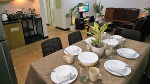 Un comedor con una mesa dispuesta para cuatro, una cocina con electrodomésticos modernos y una sala de estar con sofá y televisión.