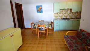 A compact kitchen with a dining table and chairs, a sofa, and a yellow cabinet.