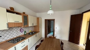 Une cuisine avec une table et des chaises en bois, une cuisinière à gaz et un luminaire suspendu.