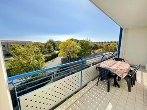 A balcony with a table and chairs, a blue railing, and a view of trees and buildings.