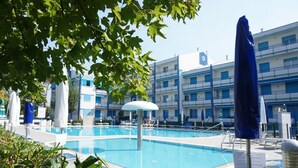 Una piscina amb gandules i ombrel·les, envoltada d'edificis amb balcons.