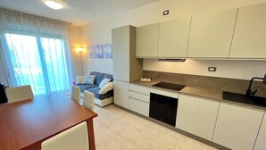 Una cuina moderna amb armaris blancs, rentaplats integrat i zona de dinar amb taula de fusta i cadires blanques.