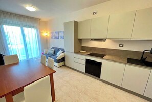 A modern kitchen with white cabinets, a black dishwasher, and a dining area with a wooden table and white chairs.
