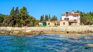 A coastal property with a stone wall, clear blue waters, and a building with multiple windows and a red roof. - Beachfront Escape in Rovinj (Rovinj)