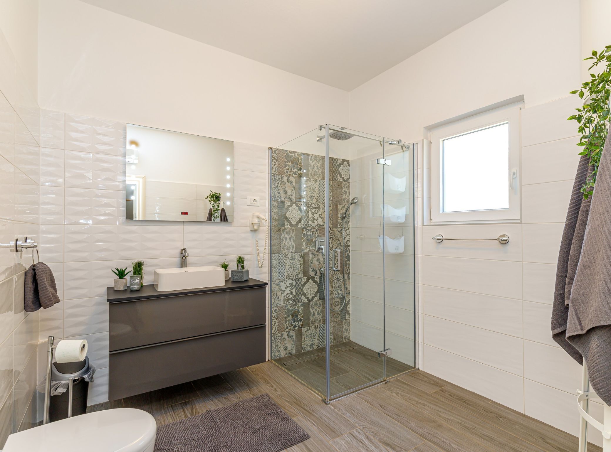 A modern bathroom with a glass shower enclosure, a white sink, and a large mirror.
