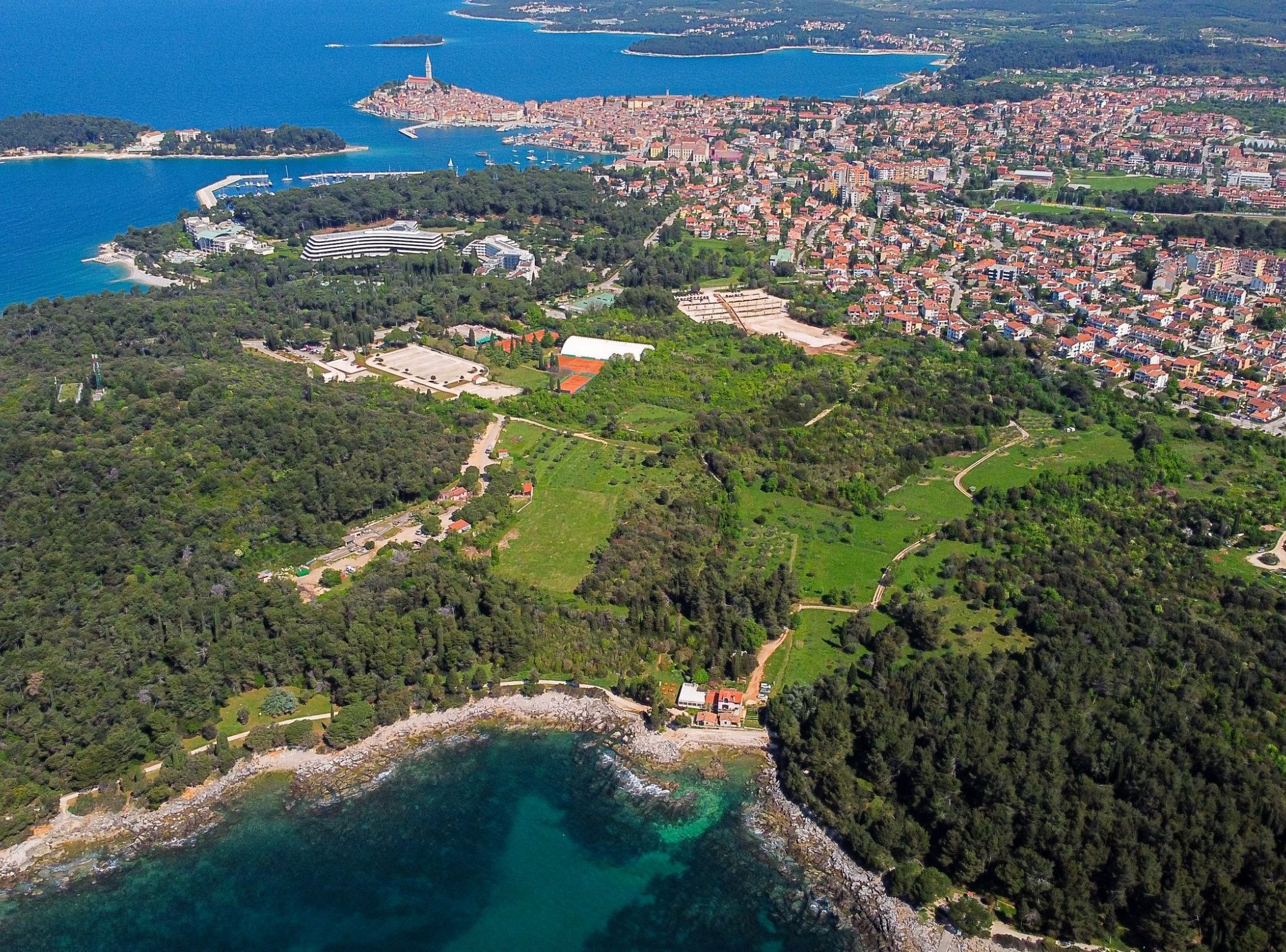 An aerial view of a coastal town with a mix of residential buildings, green spaces, and a marina.