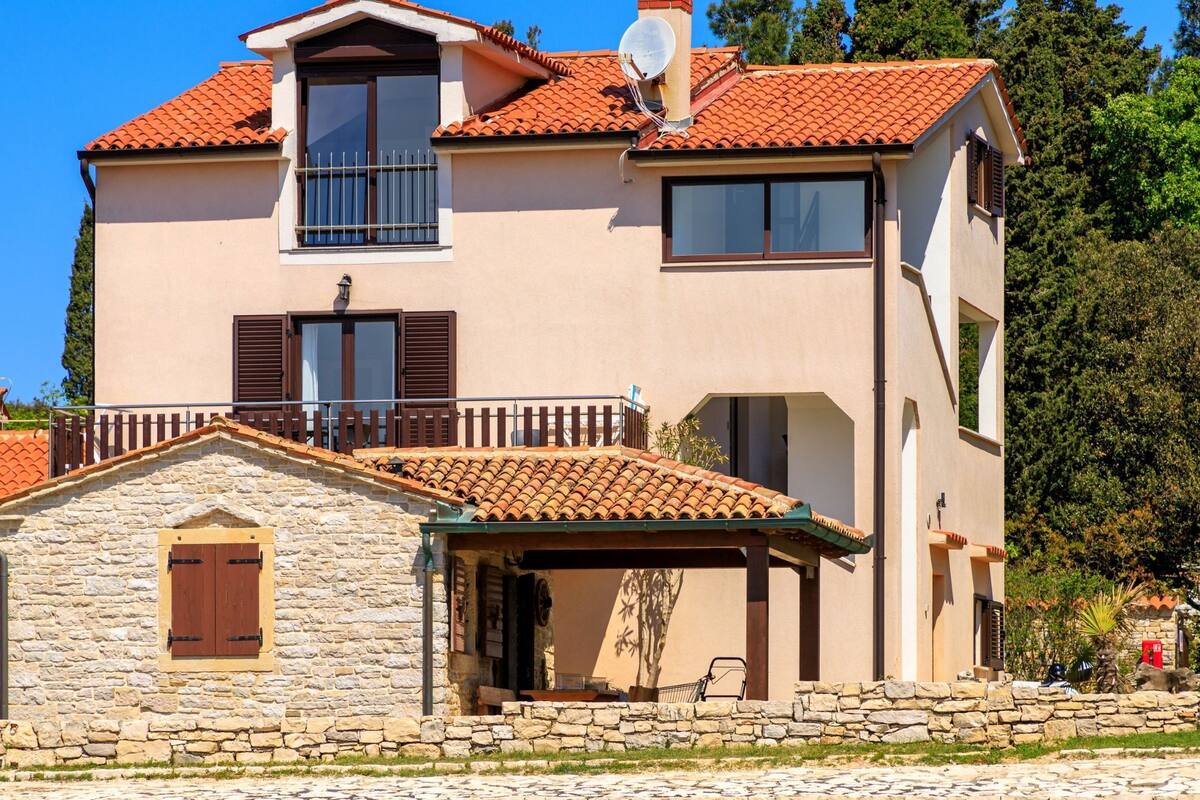 A two-story house with a stone facade, a tiled roof, and a balcony.