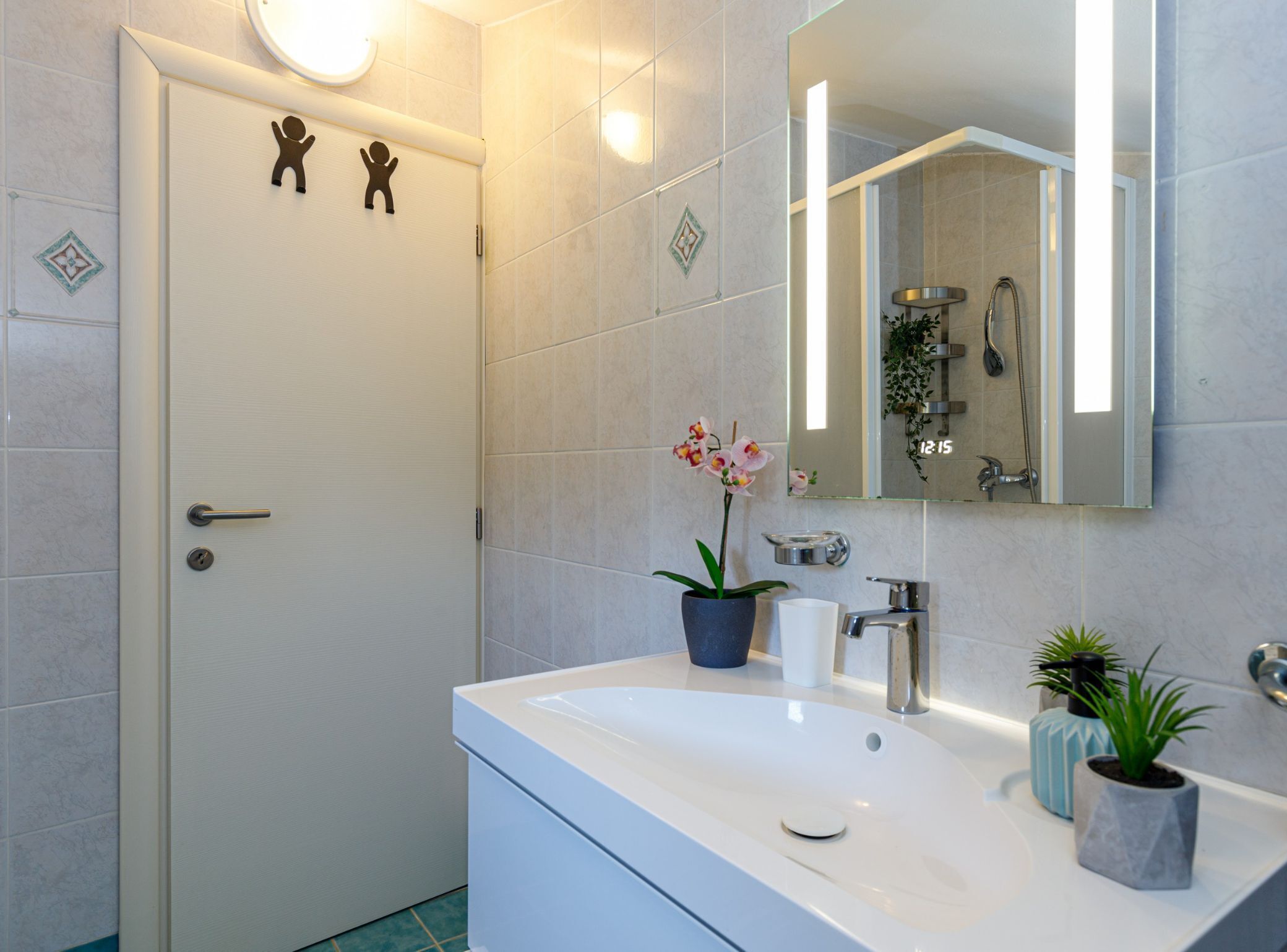 Une salle de bain moderne avec un lavabo blanc, un miroir et une porte dotée d’un interrupteur.
