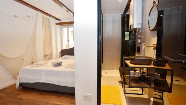 Een moderne slaapkamer met een bed, een badkamer met een wastafel en spiegel, en een douche.