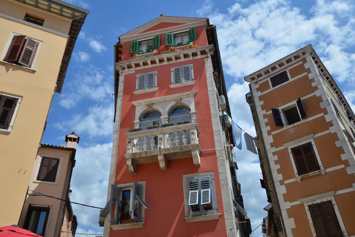 Um edifício de vários andares com varandas, fachada vermelha e persianas tradicionais.