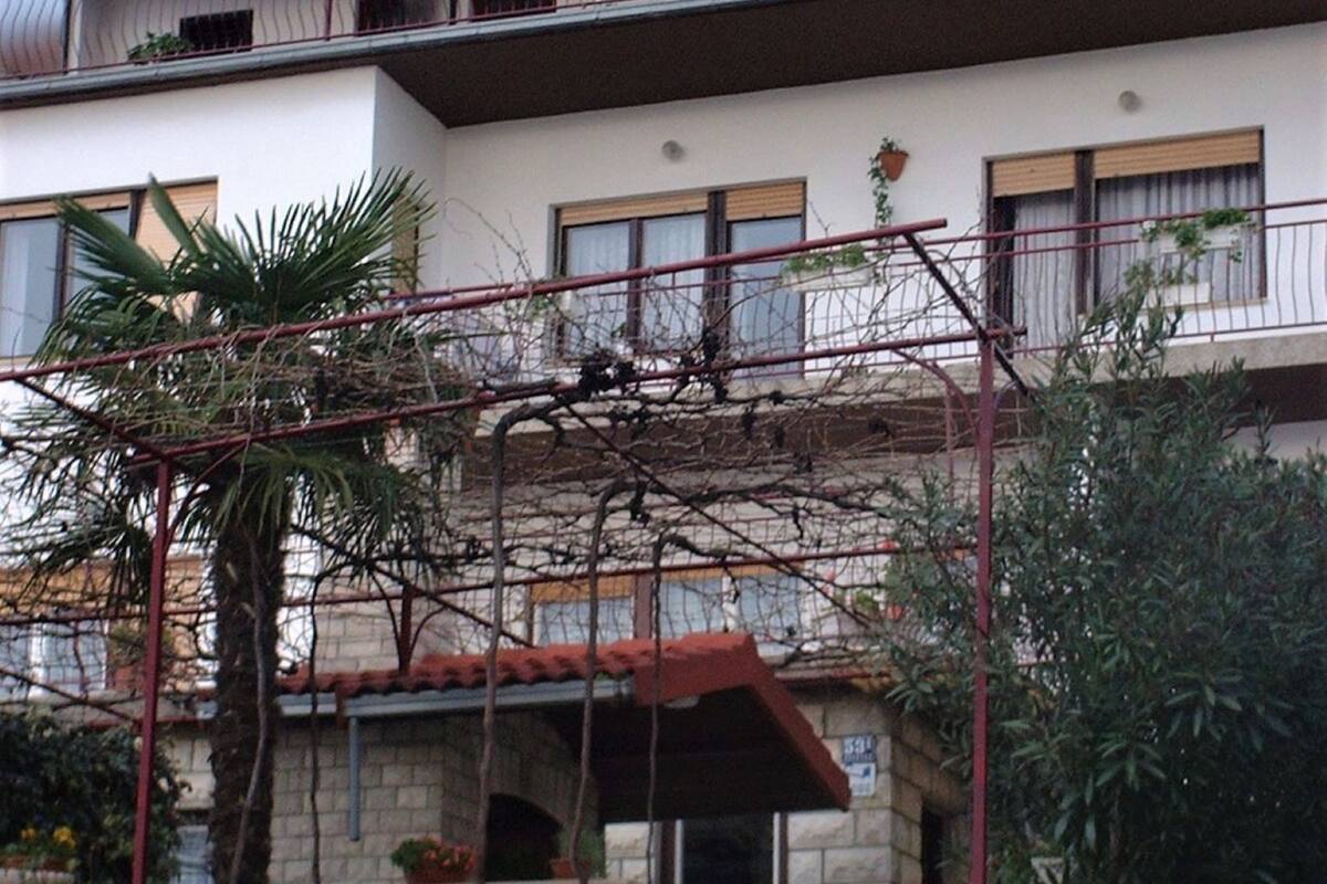A multi-story building with a stone facade, balconies, and a small garden area with potted plants.