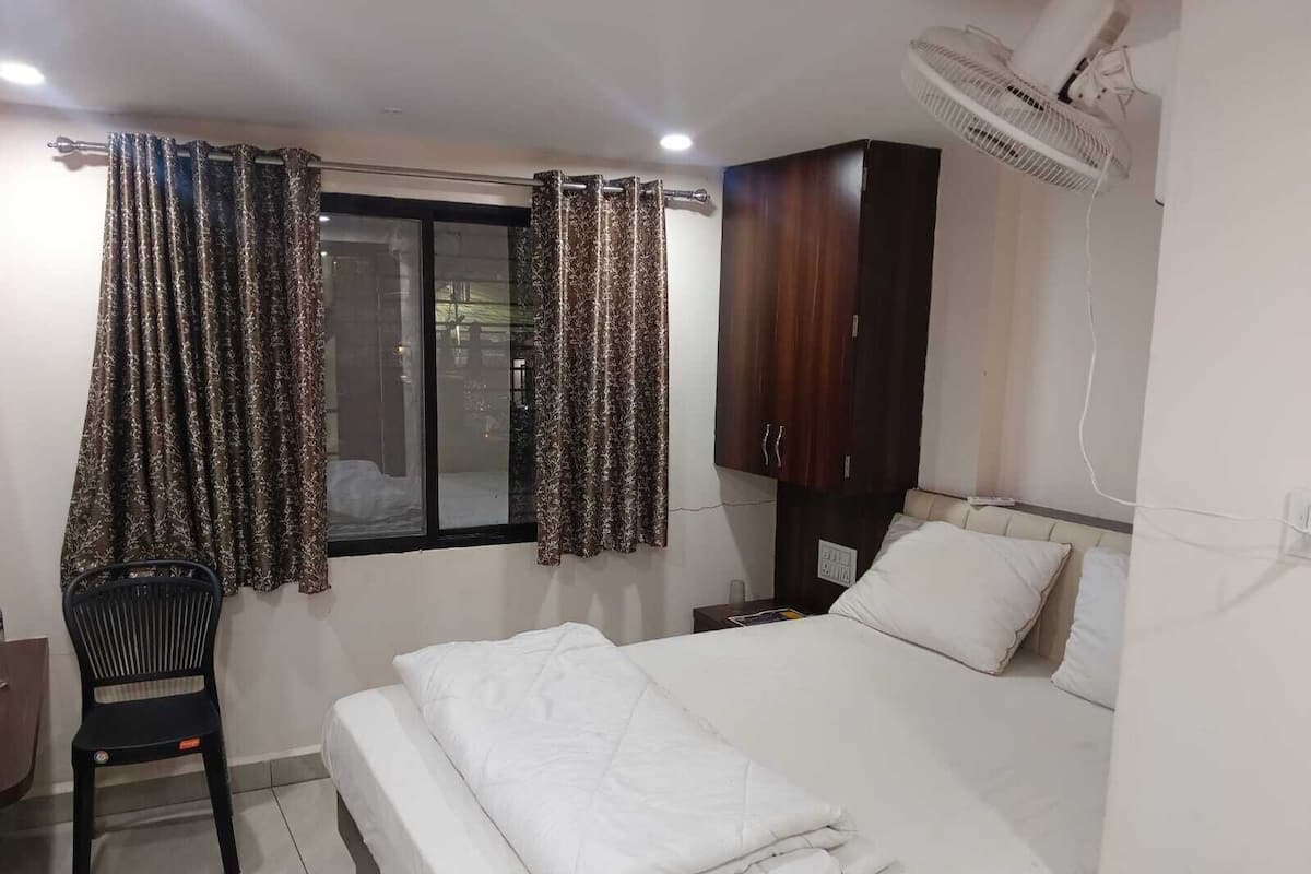 A bedroom with a bed, a chair, a wardrobe, a window with curtains, and a ceiling fan.