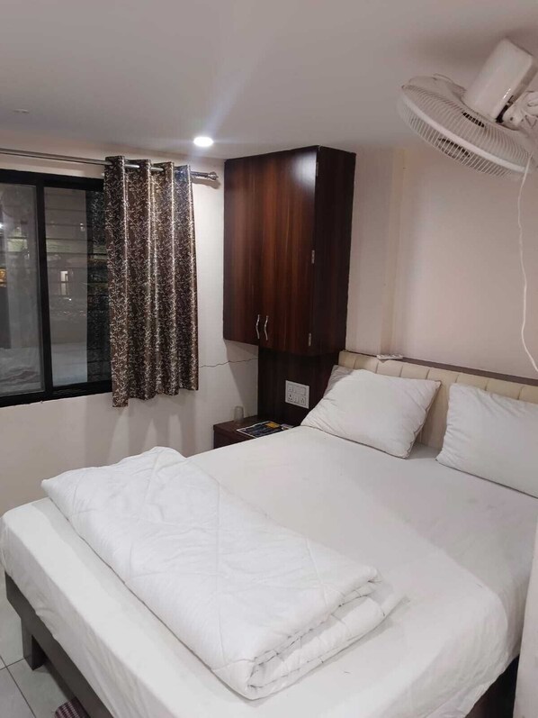 A hotel room with a bed, a wooden wardrobe, a bedside table with a lamp, and a window with curtains.
