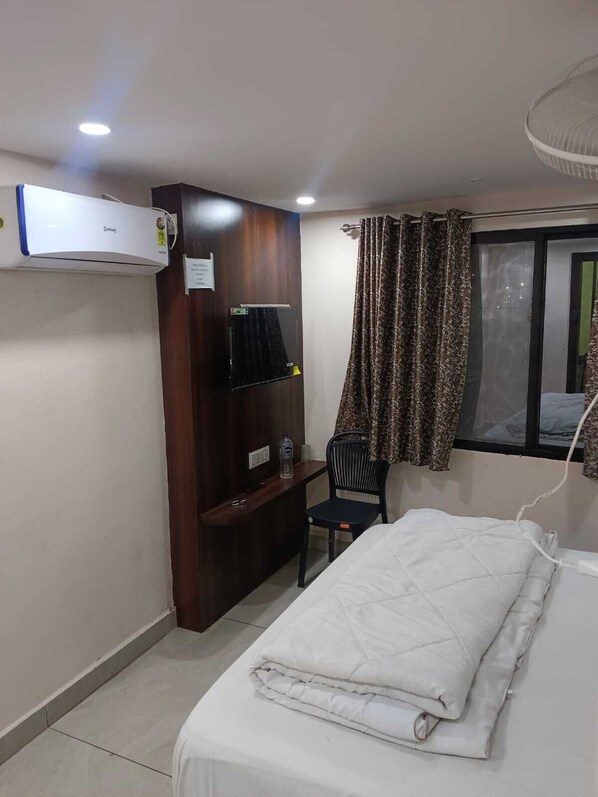 Una habitación de hotel con cama, escritorio, silla, aire acondicionado y ventana con cortinas.