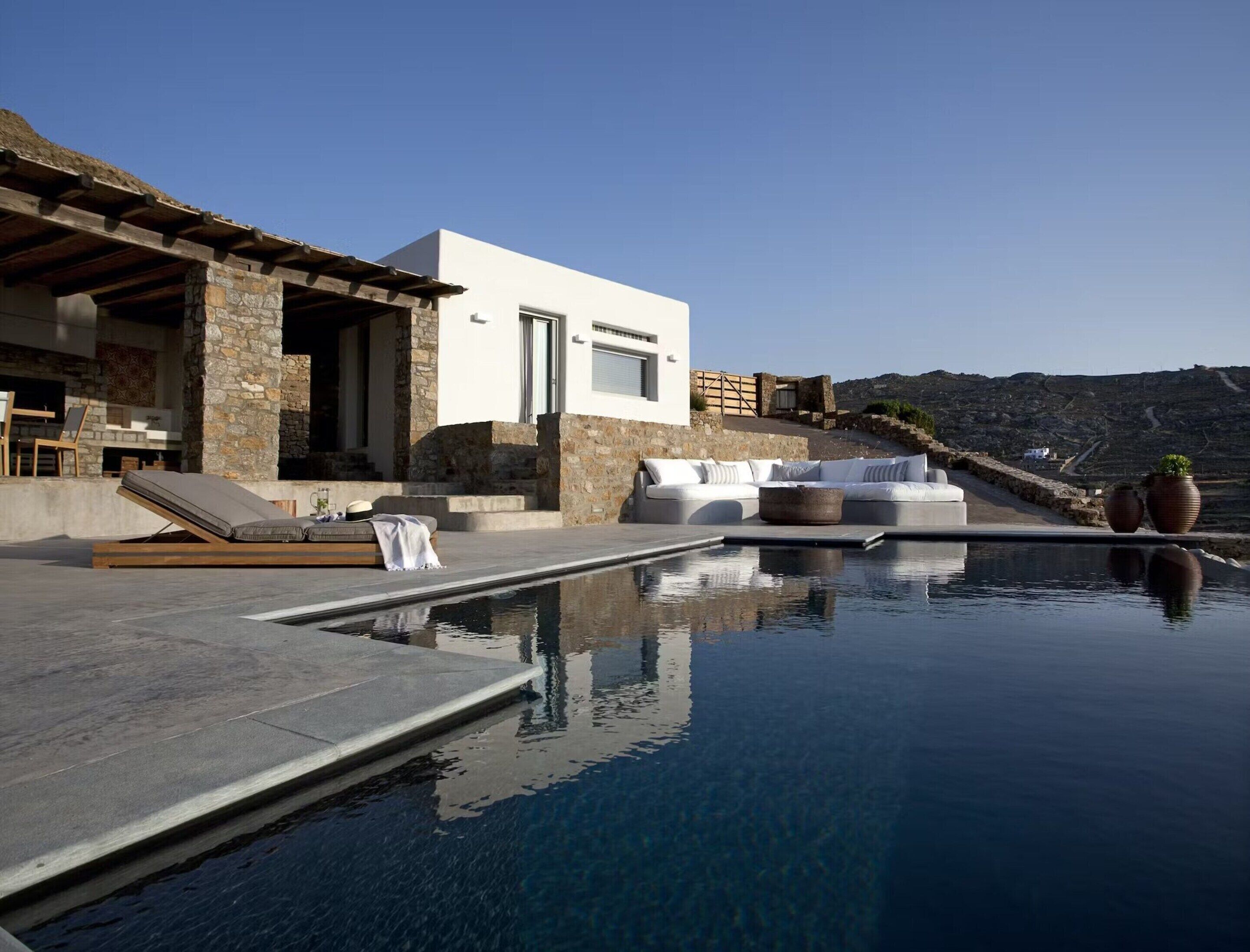 A modern outdoor pool area with a stone structure, a white building, and a view of the landscape.