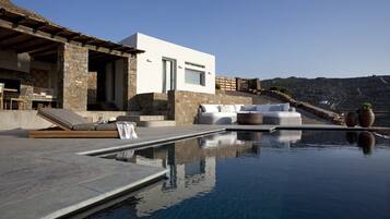 A modern outdoor pool area with a stone structure, a white building, and a view of the landscape.