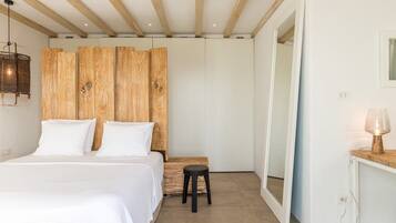 A bedroom with a bed, wooden headboard, a small stool, a bedside table with a lamp, and a mirror.