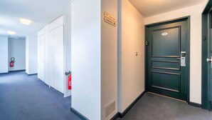 A hallway with white walls, a fire extinguisher, a door with a number plate, and directional signs. - Charming Studio- 2P- Jardin des Plantes/austerlitz (Paris)