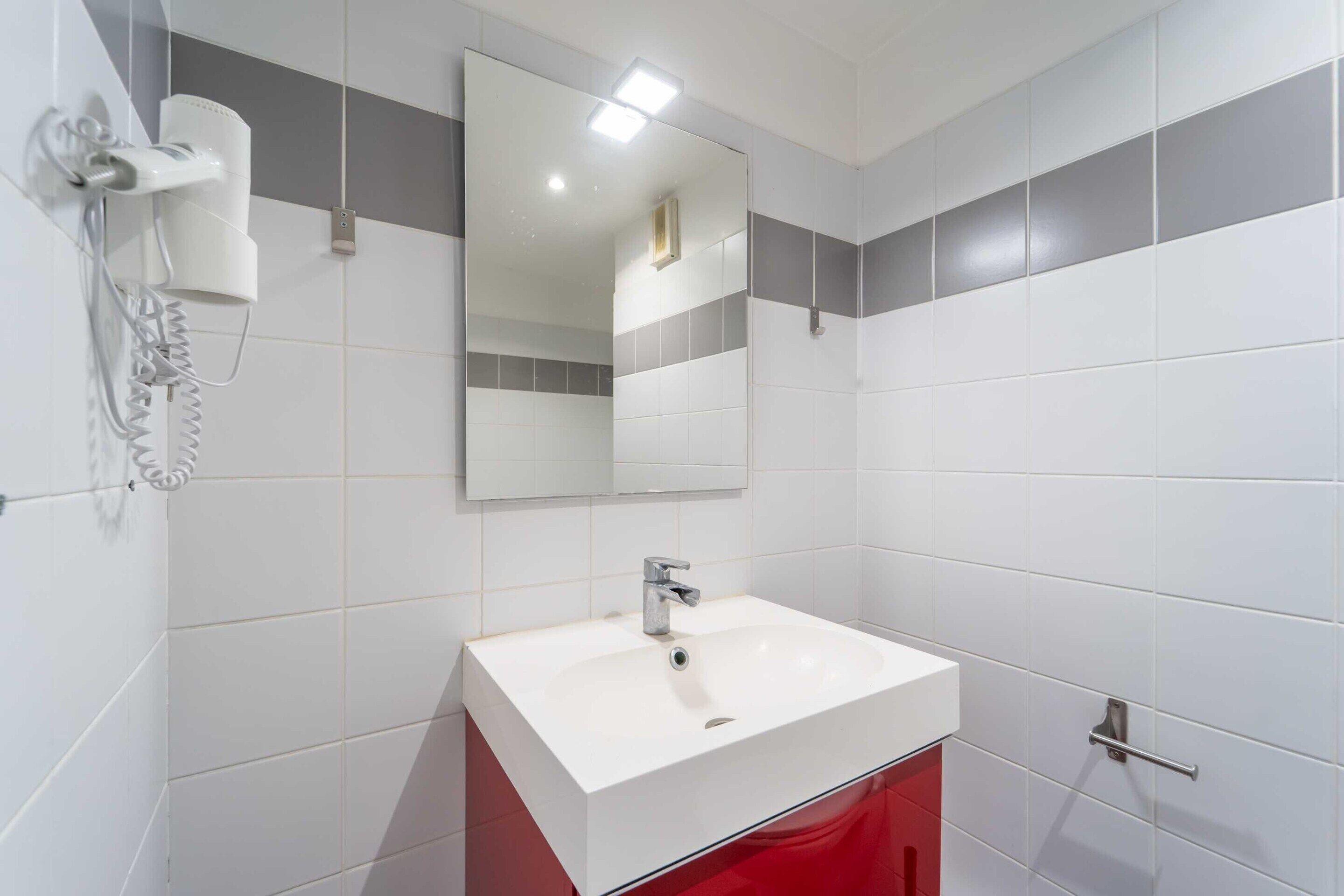 A bathroom with a white sink, a mirror, and a hairdryer mounted on the wall.