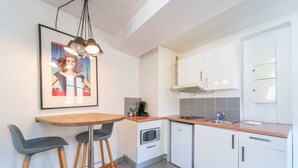 A modern kitchen with white cabinets, a wooden countertop, a built-in microwave, and a small refrigerator. There is a bar stool and a framed picture on the wall. - Charming Studio- 2P- Jardin des Plantes/austerlitz (Paris)
