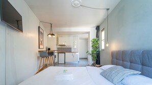 A compact hotel room with a bed, bedside table, and a small kitchenette in the background. - Charming Studio- 2P- Jardin des Plantes/austerlitz (Paris)