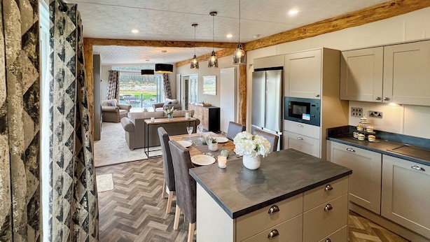 A modern kitchen with a herringbone floor pattern, wooden beams, and a central island with seating.