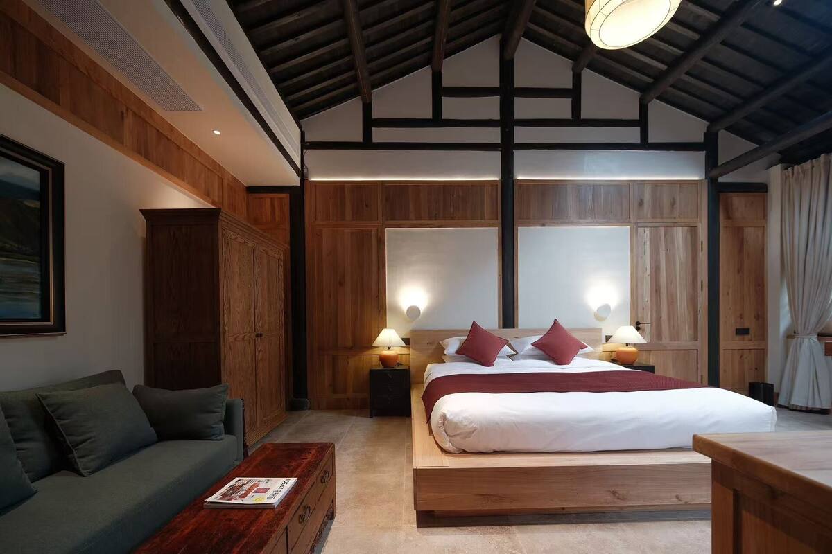 A modern hotel room with a wooden ceiling, a large bed with red pillows, a green sofa, and a wooden coffee table.