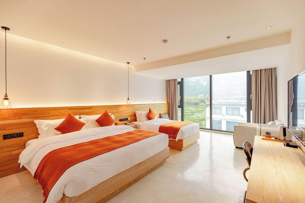 A modern hotel room with two beds, a desk, and a large window offering a city view.