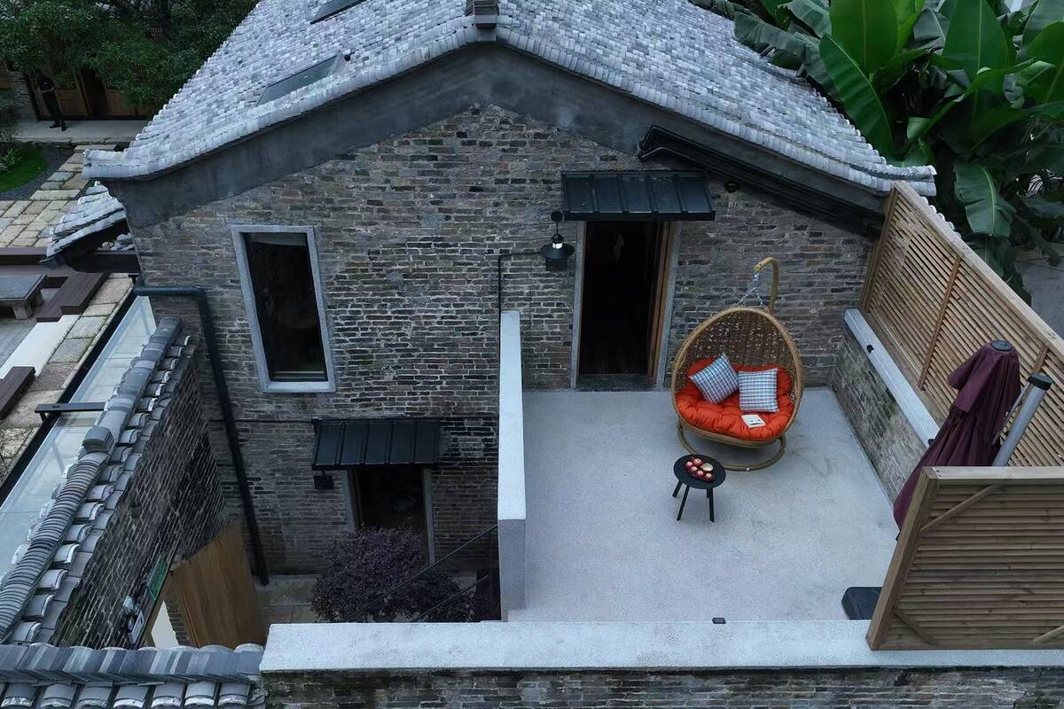A traditional stone building with a small balcony, a hanging chair, and a small table with fruit.
