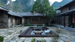 A courtyard with traditional architecture, stone paving, and a central seating area with a table and benches. - See You in the mountains (Guilin)