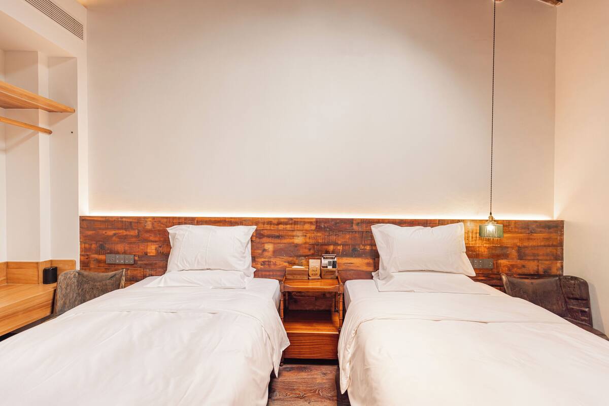 A hotel room with two beds, wooden headboard, bedside tables, and a hanging light fixture.