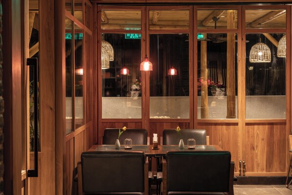 A restaurant with wooden paneled walls, a glass door entrance, and a table set for two with chairs. - See You in the mountains (Guilin)