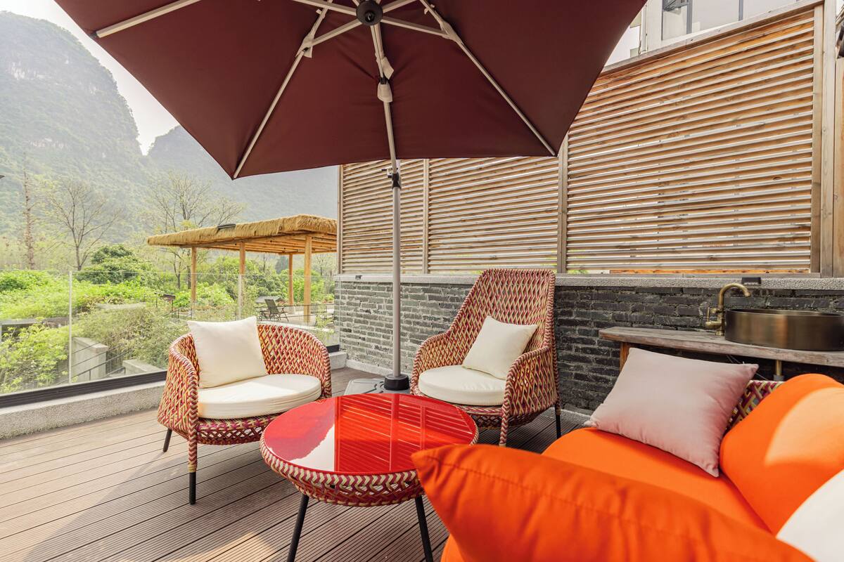 A balcony with wicker chairs, a red table, and a large umbrella.