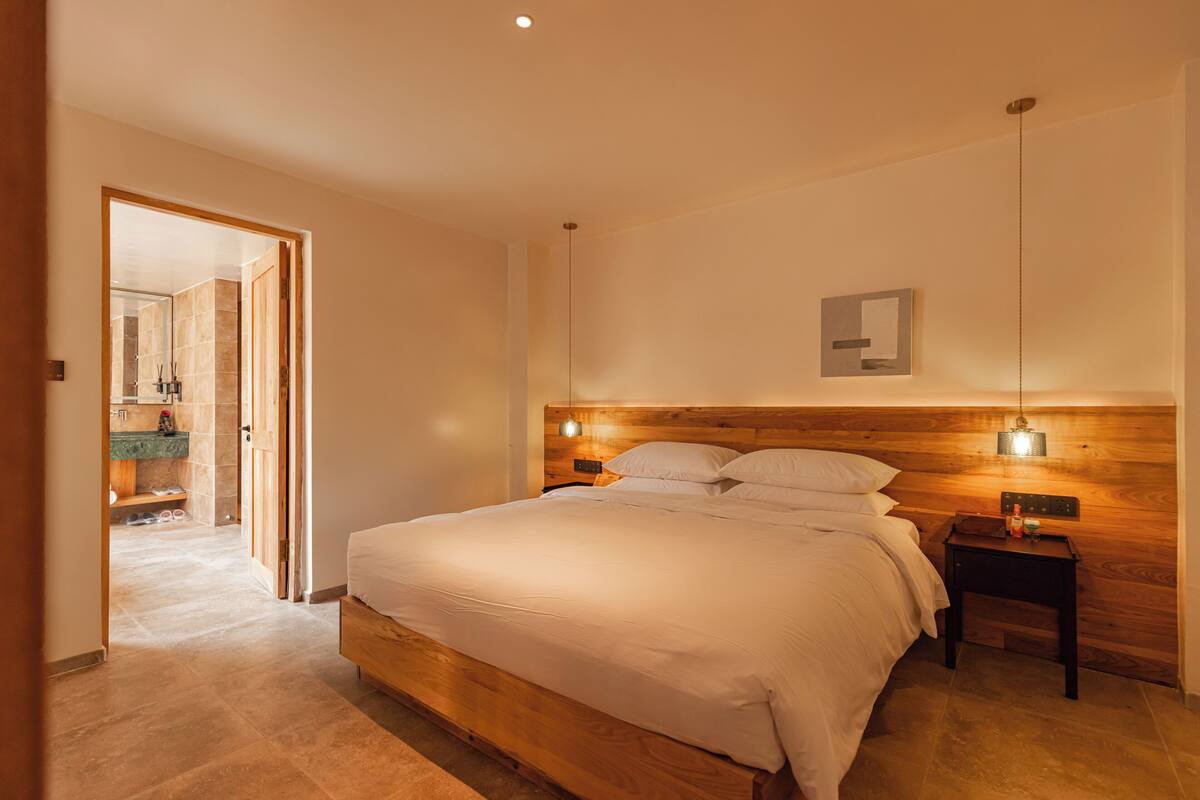 A bedroom with a wooden headboard, a bed with white linens, two bedside tables with lamps, and a wooden floor.