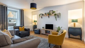 A modern living room with a sofa, armchairs, a TV, and decorative shelves.