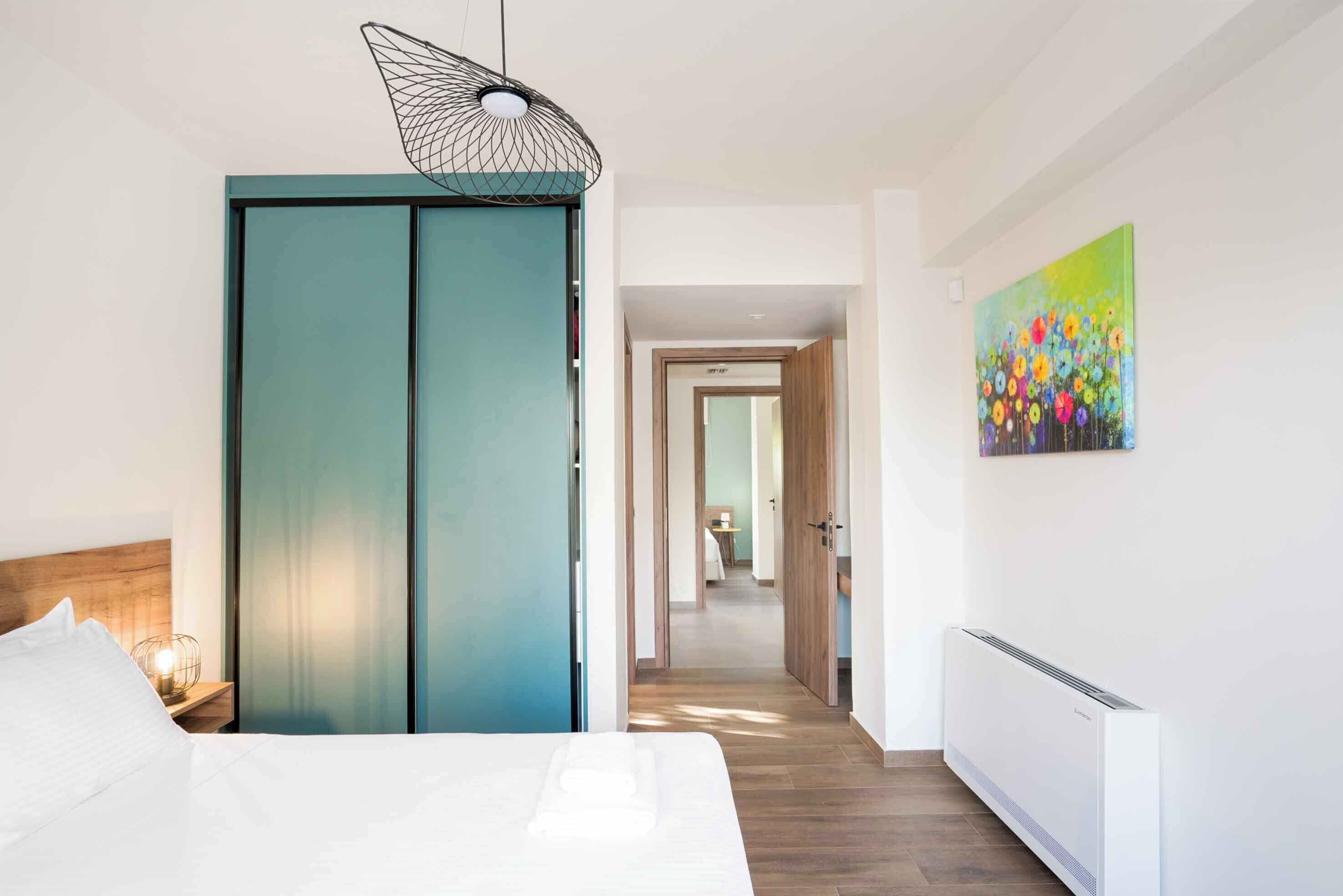 A modern bedroom with a bed, a wardrobe, a painting, and a hallway leading to another room.