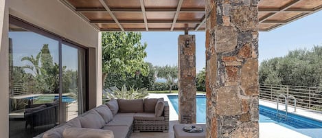 Un área de estar al aire libre techada con piscina, pilares de piedra y vistas del paisaje circundante.