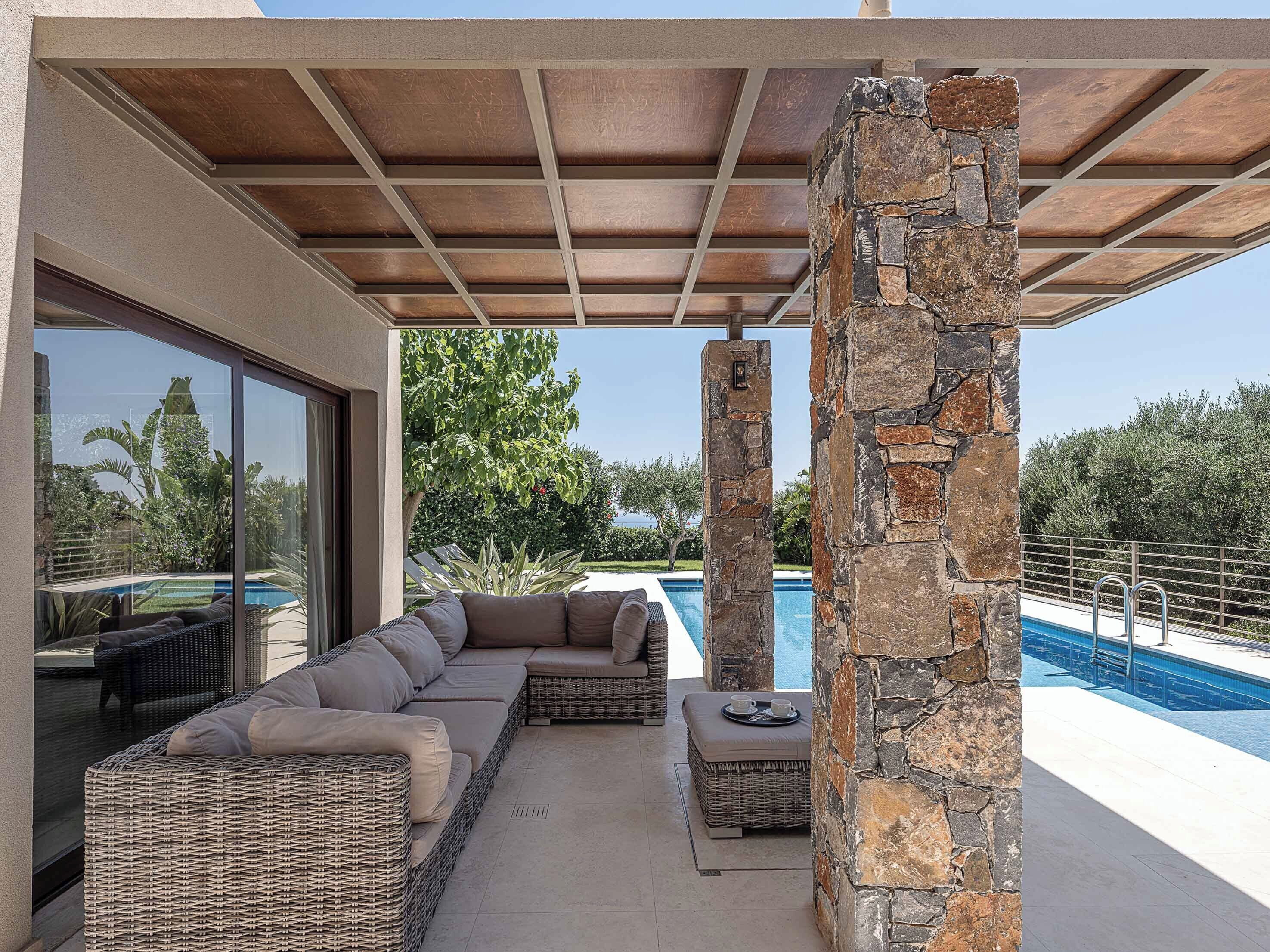 Un espace extérieur aménagé, abrité et doté de sièges, avec une piscine, des piliers en pierre et une vue sur le paysage environnant.