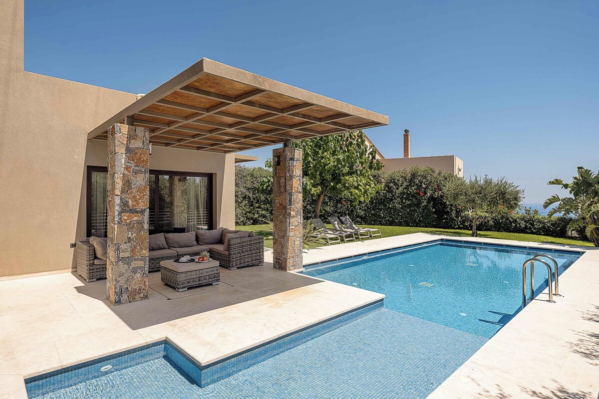 A swimming pool with a pergola, outdoor seating, and a view of a building in the background.
