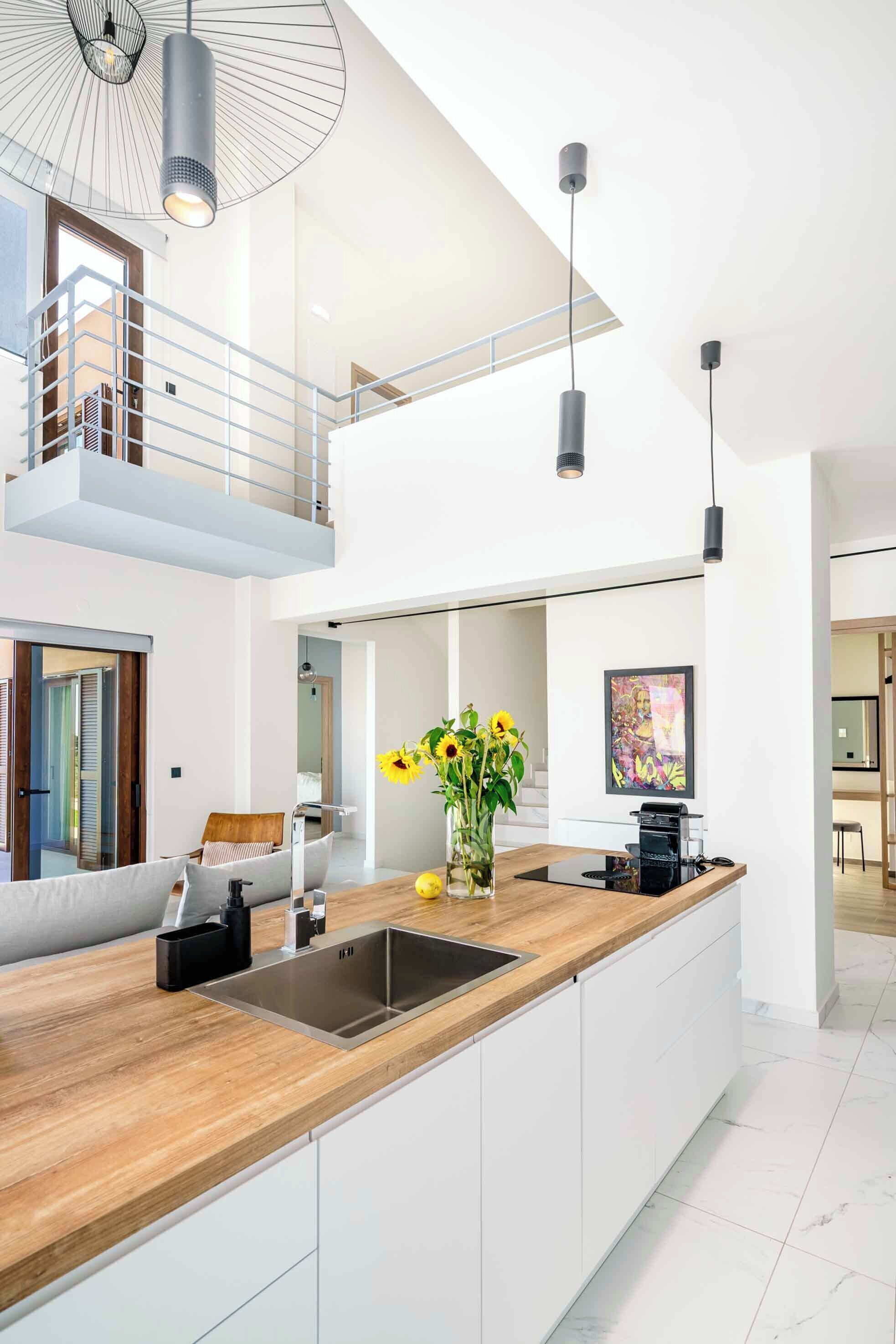 A modern kitchen with a wooden countertop, stainless steel sink, and pendant lighting.