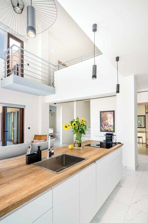 A modern kitchen with a wooden countertop, stainless steel sink, and pendant lighting. - Olimpia Villas - Holiways Collection (Apokoronas)