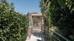 A pathway leading to a stone structure with a metal gate, surrounded by dense foliage. - Olimpia Villas (Apokoronas)